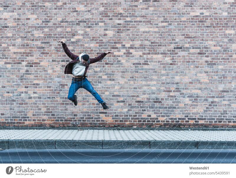 Young man jumping in front of brick wall Leaping men males jumps Adults grown-ups grownups adult people persons human being humans human beings pavement