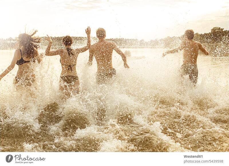 Four friends running into quarry pond splashing enjoying enjoyment indulgence indulging together side by side paralell in paralell motion moving Move youth