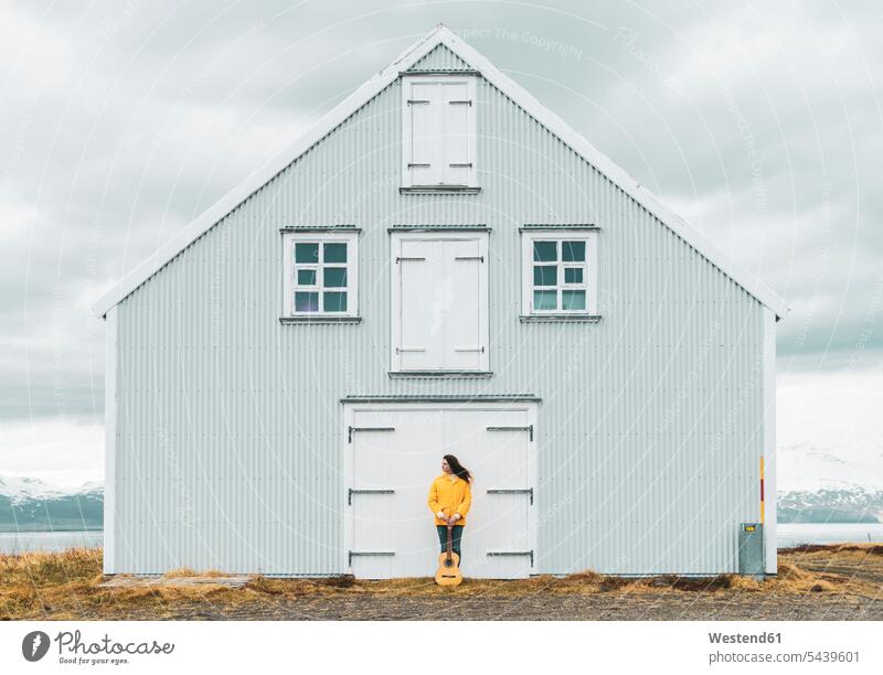 Iceland, woman with guitar standing at lonely house females women houses secluded guitars Adults grown-ups grownups adult people persons human being humans