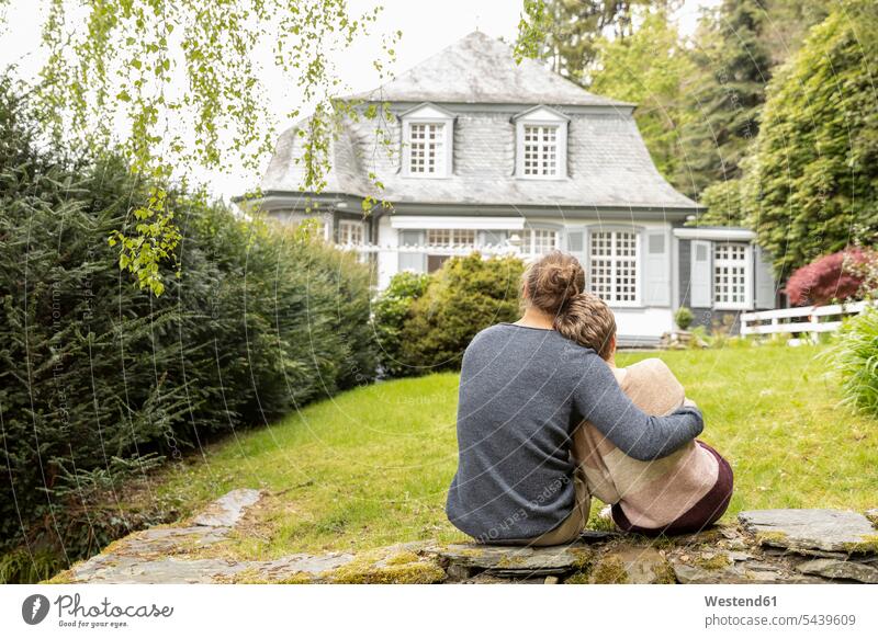 Rear view of couple sitting on a wall in garden jumper sweater Sweaters Seated embrace Embracement hug hugging relax relaxing relaxation enjoy enjoyment