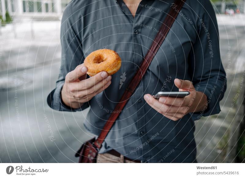 Hands of businessman holding doughnut and smartphone, Partial view donuts Doughnuts Smartphone iPhone Smartphones hand human hand hands human hands Businessman