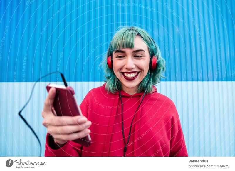 Portrait of laughing young woman with blue dyed hair with headphones taking selfie with smartphone coloured Smartphone iPhone Smartphones Laughter portrait