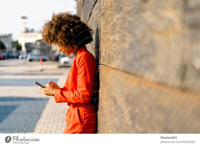 Young woman wearing fashionable red pantsuit leaning against wall using cell phone human human being human beings humans person persons Mixed Race