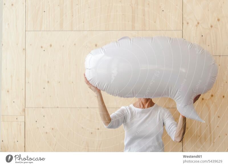 Woman standing in office, holding inflatable speech bubble in front of her face blow-up speech balloon thought bubble obscured face obscured faces face hidden