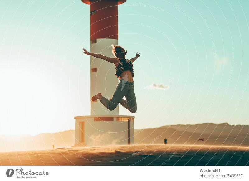 Young woman jumping in desert landscape at lighthouse lighthouses light houses Leaping Deserts females women landscapes scenery terrain tower towers