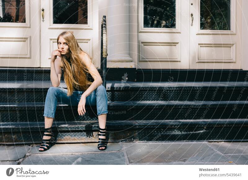 USA, New York City, pensive young woman sitting on stairs in front of an entry door caucasian european caucasian ethnicity caucasian appearance finger on mouth