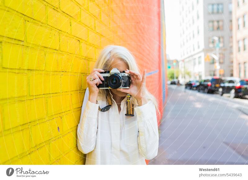 Mature woman leaning against wall taking picture with camera females women photographing Adults grown-ups grownups adult people persons human being humans