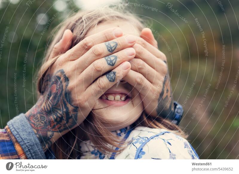 Man's tattooed hands covering eyes of his daughter 6-7 years 6 to 7 6 to 7 years smiling smile bonding community Joy enjoyment pleasure outdoors location shot