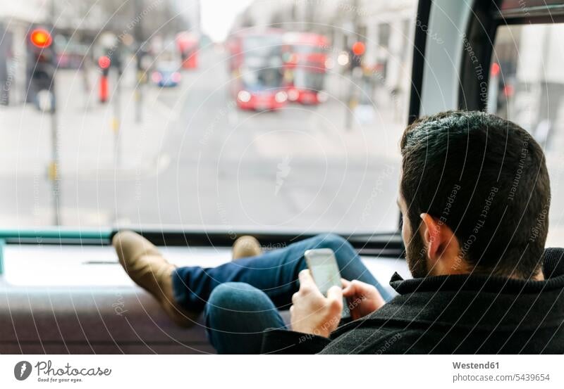 UK, London, young man in a double-decker bus using his smartphone caucasian caucasian ethnicity caucasian appearance european on the move on the way on the go