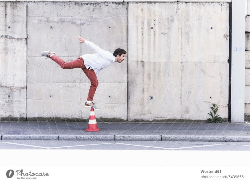 Young man balancing on traffic cone in front of concrete wall Acrobatic Activity human human being human beings humans person persons caucasian appearance
