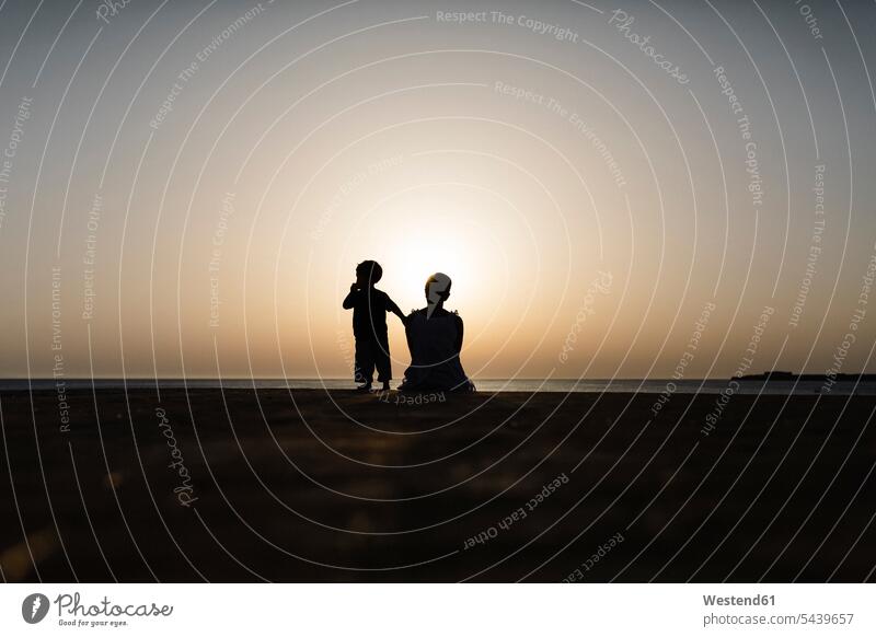 Spain, Menorca, silhouette of mother and son watching the sunset at seafront surface level worm's eye view nature Travel destination Travel destinations