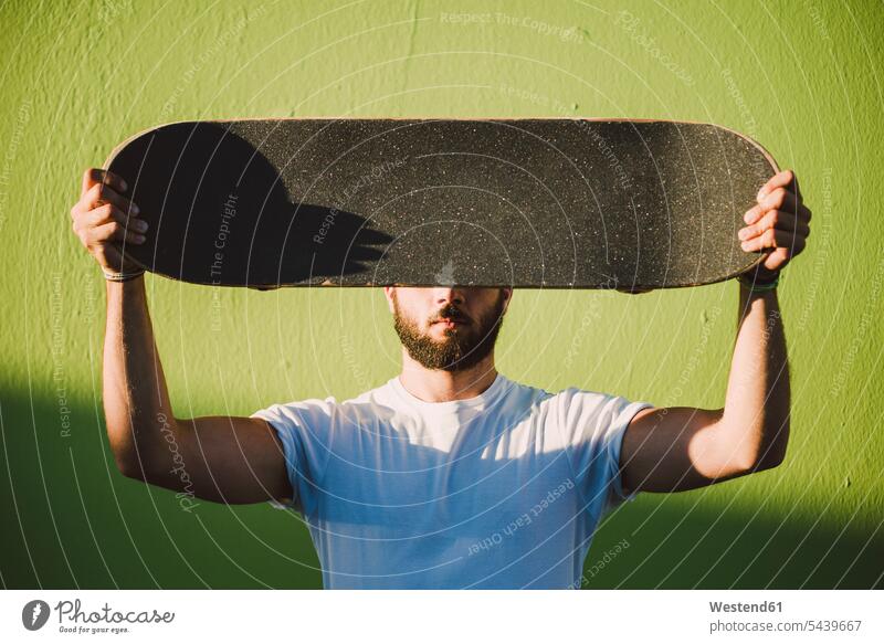 Man holding on his skateboard in front of his face skateboarder skater skateboarders skaters people persons human being humans human beings men males Adults