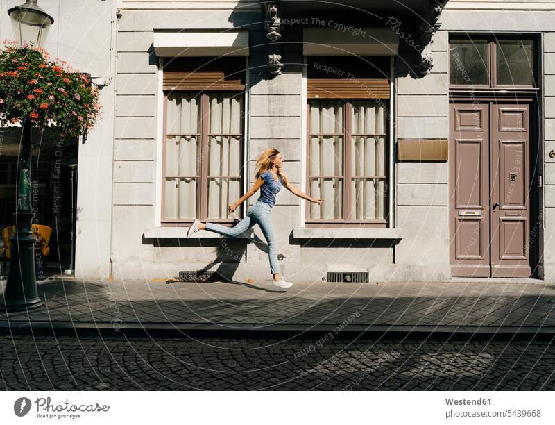 Netherlands, Maastricht, blond young woman running along building in the city town cities towns blond hair blonde hair females women house houses outdoors