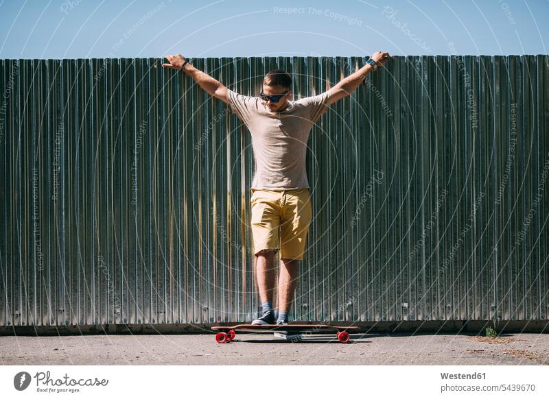 Young man with longboard standing at a wall skateboard Skate Board skateboards men males Adults grown-ups grownups adult people persons human being humans