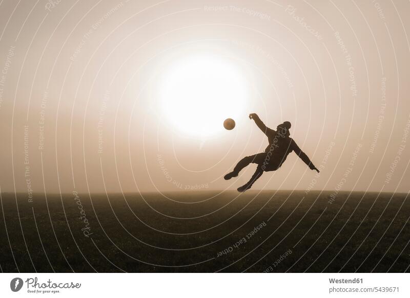 Young man playing soccer on meadow in the evening caucasian caucasian ethnicity caucasian appearance european soccer ball soccer balls footballs Sun silhouette