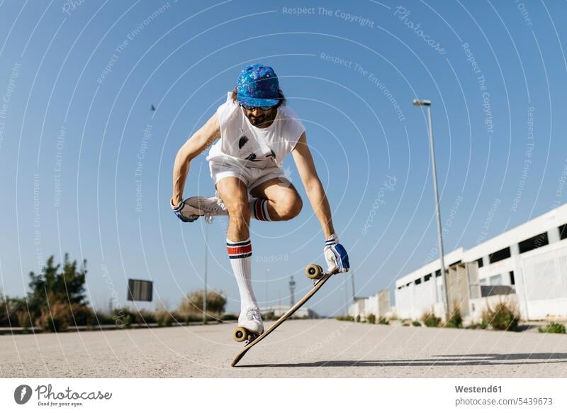 Man in stylish sportive outfit standing on skateboard against blue sky Trick skateboarder skater skateboarders skaters skateboarding man men males sporting