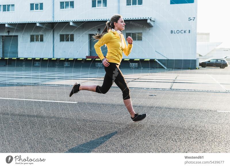 Young woman running on a street females women Jogging road streets roads Adults grown-ups grownups adult people persons human being humans human beings fitness
