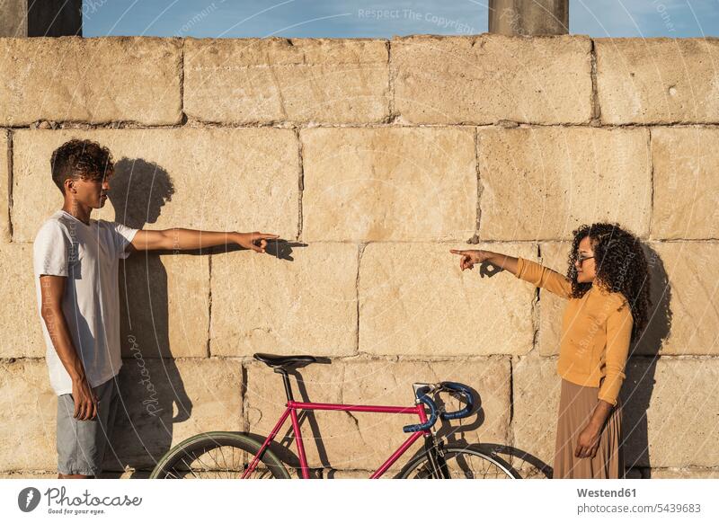 Young couple standing in front of wall, pointing at eachother human human being human beings humans person persons Mixed Race mixed race ethnicity