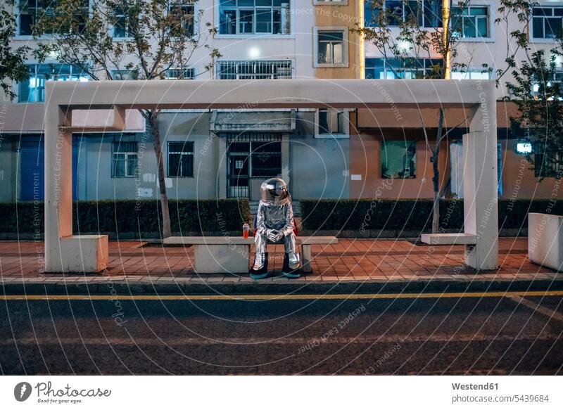 Spaceman sitting on bench at a bus stop at night with soft drink busstops spaceman spacemen by night nite night photography astronaut astronauts