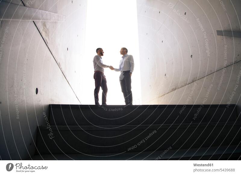 Two businessmen shaking hands in a passageway Businessman Business man Businessmen Business men colleagues Handclasp Handclap business people businesspeople
