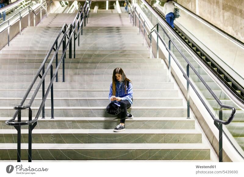 Young woman sitting on stairs using cell phone and earphones Smartphone iPhone Smartphones use females women Seated ear phone ear phones mobile phone mobiles