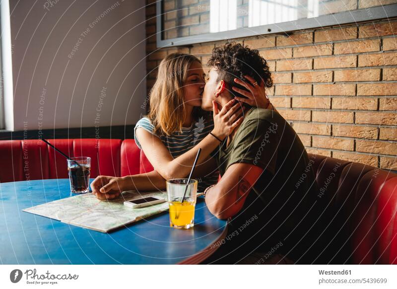 Young couple with map kissing in a cafe sitting Seated maps Table Tables kisses twosomes partnership couples people persons human being humans human beings
