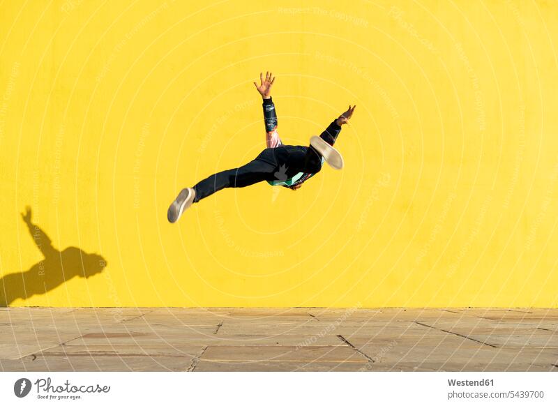 Acrobat jumping somersaults in front of yellow wall walls Somersaulting Flip acrobat acrobats equilibrists Leaping acrobatics Acrobatic Activity sport sports