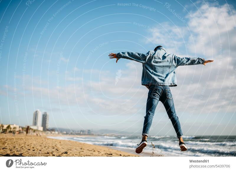 Spain, Barcelona, back view of young man jumping in the air on the beach beaches men males Leaping Adults grown-ups grownups adult people persons human being