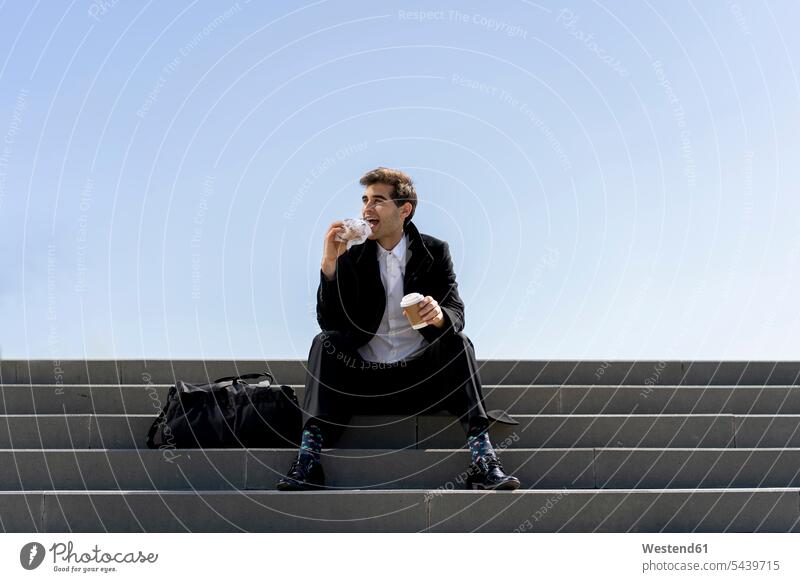 Businessman sitting on stairs having lunch break Barcelona disposable cup disposable cups coffee break doughnut donuts Doughnuts steps clear sky copy space