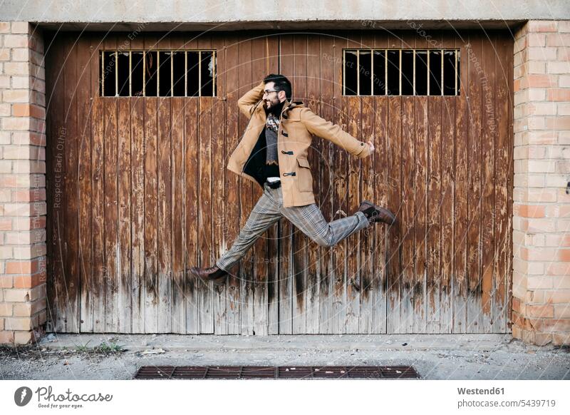 Spain, Igualada, happy man jumping mid-air at rundown wooden gate Run Down disrepair Run-Down Town wooden door woden doors Leaping men males happiness jumps