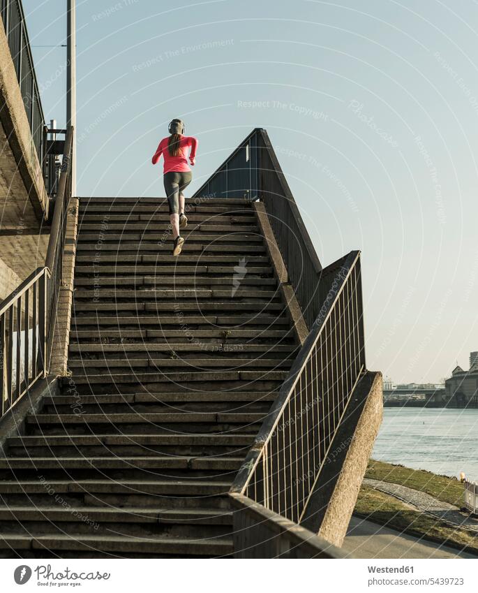 Young woman running up stairs at a river Jogging upwards females women River Rivers stairway fitness sport sports Adults grown-ups grownups adult people persons