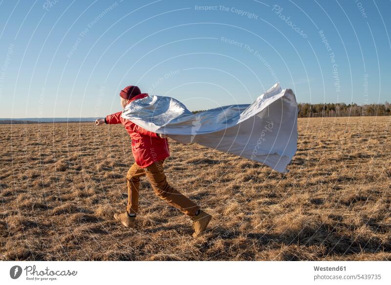 Boy dressed up as superhero running in steppe landscape Russia Russian Federation playful vastness wide Broad Far copy space wideness clear sky cloudless