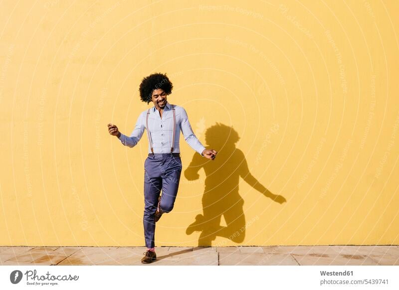 Smiling man dancing in front of yellow wall men males walls dance smiling smile Adults grown-ups grownups adult people persons human being humans human beings