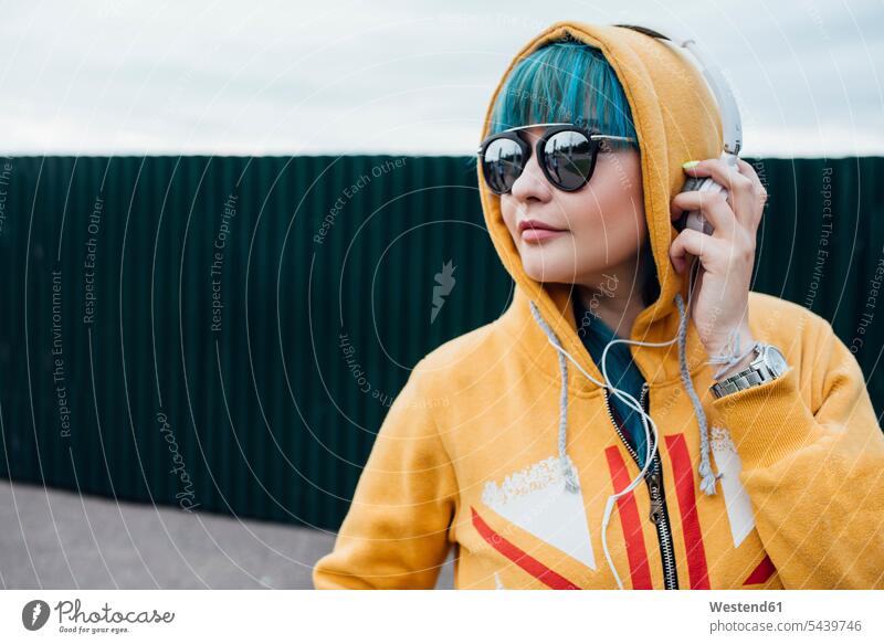 Portrait of young woman with dyed blue hair listening music with headphones hearing portrait portraits females women coloured headset colours people persons