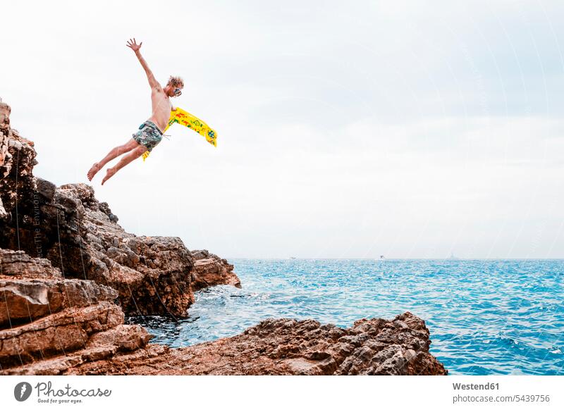 Man with airbed jumping from rock into the sea Leaping ocean man men males jumps water waters body of water Adults grown-ups grownups adult people persons