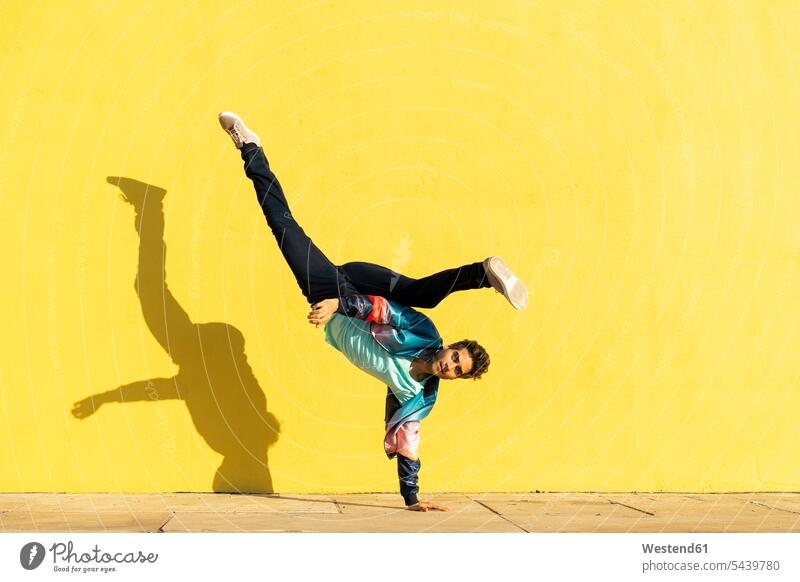 Acrobat doing movement training in front of a yellow wall practicing practice practise exercise exercising practising self realization self-realisation