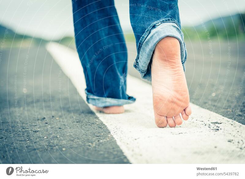 Young woman walking barefoot on centre line of empty street, partial view caucasian european caucasian ethnicity caucasian appearance going copy space tarmac