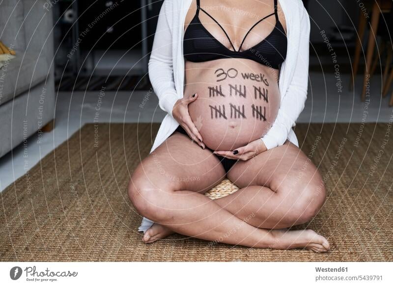 Close-up of pregnant woman sitting on the floor at home with tally marks on her belly bellies stomach stomachs floors females women Pregnant Woman Seated