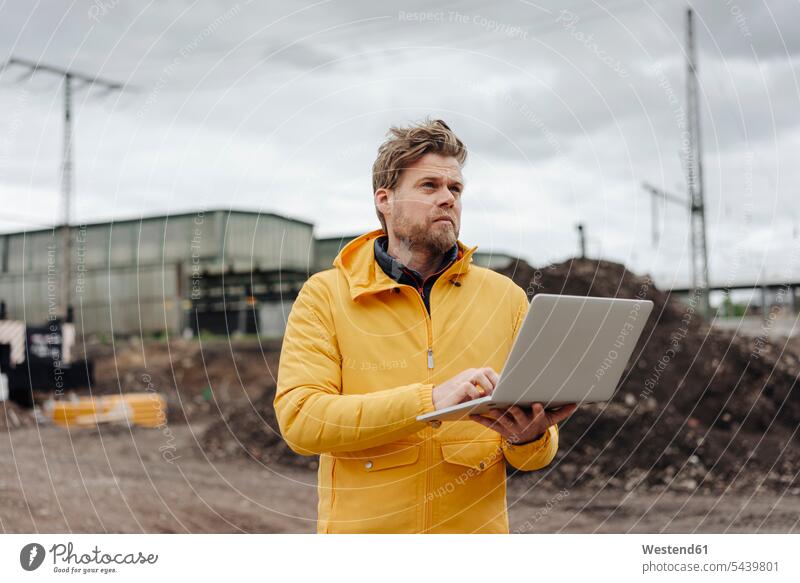 Man holding laptop, construction site in the background expertise competence competent engineer engineers Job Occupation Work Laptop Computers laptops notebook