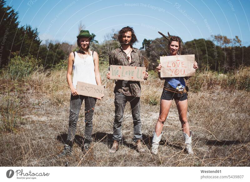 Three hippies holding 'I love you' signs in the nature barren land wasteland natural world smiling smile amiable likeable casual leisure wear casual clothing