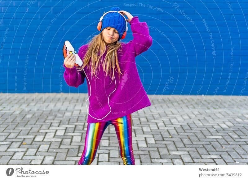 Portrait of girl dancing outdoors while listening music with headphones and smartphone Spain Smartphone iPhone Smartphones fashionable childhood woolly hat