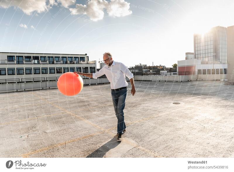 Mature man playing with orange fitness ball on rooftop of a high-rise building copy space sky skies modern contemporary cloud clouds day daylight shot