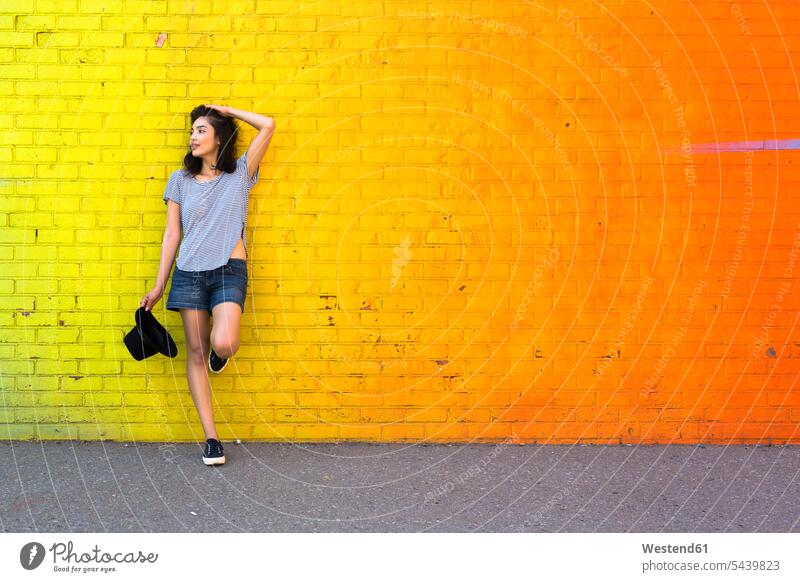 Young woman leaning against yellow brick wall Latin American and Hispanic Ethnicity on one leg portrait portraits walls hat hats orange young women young woman