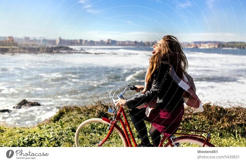 Spain, Gijon, playful young woman riding bicycle at the coast caucasian caucasian ethnicity caucasian appearance european sky skies carefree bikes bicycles