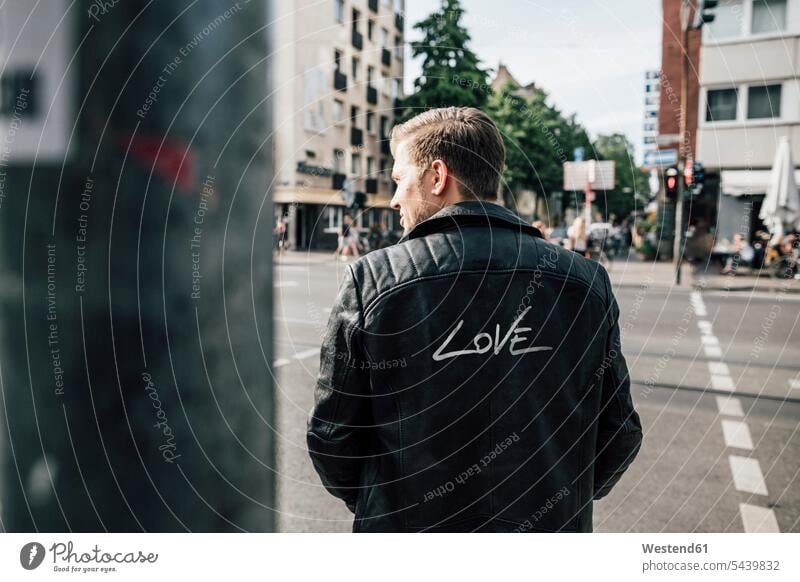 Back view of young man wearing black leather jacket with writing 'Love' leather jackets loving men males coat coats positive Adults grown-ups grownups adult
