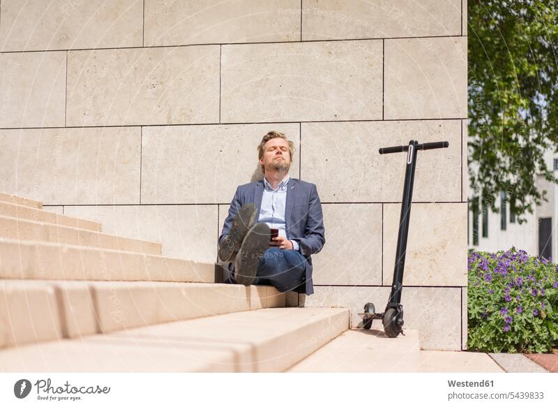Businessman with E-Scooter and smartphone sitting on steps relaxing business life business world business person businesspeople Business man Business men