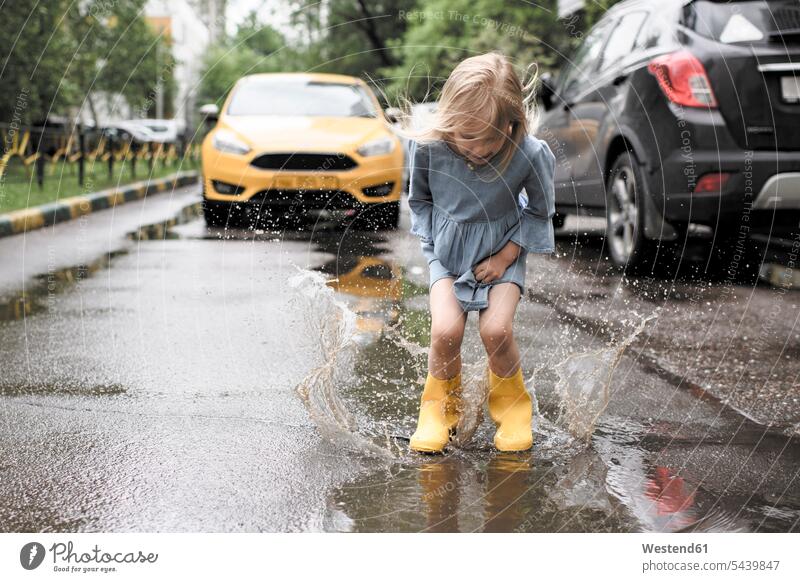 Girl wearing blue dress and rubber boots, jumping in pond on street, yellow car in the background Wellington Boot Gumboots Rubber Boot wellies Wellington Boots