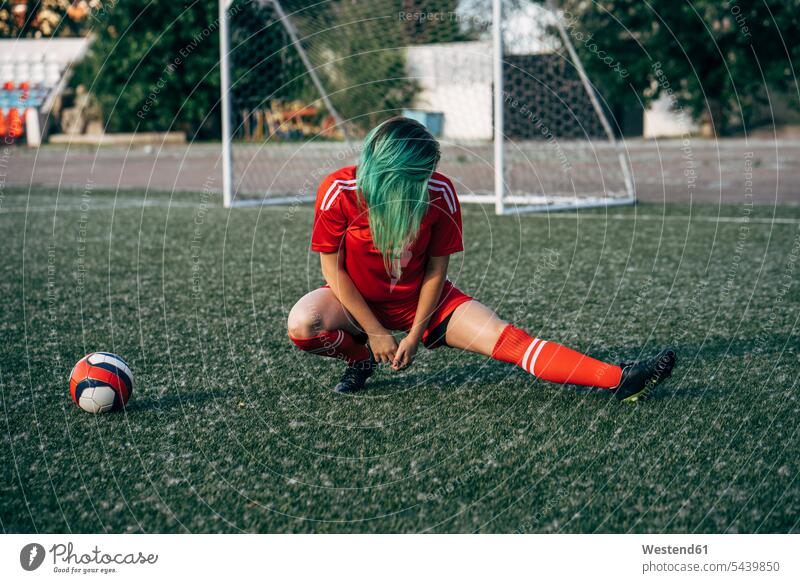 Young woman stretching on football ground next to the ball soccer pitch football pitch females women balls sport sports Adults grown-ups grownups adult people