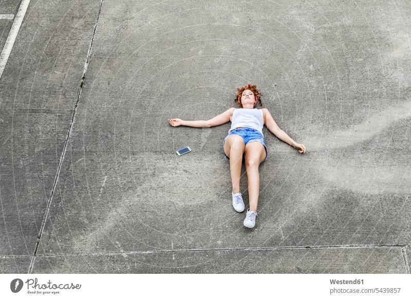 Young woman lying on parking level next to cell phone mobile phone mobiles mobile phones Cellphone cell phones females women curly hair curls laying down lie