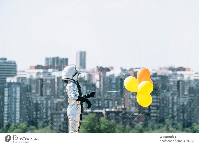 Boy dressed as an astronaut holding balloons in the city human human being human beings humans person persons braver bravers hero space travel spacemen